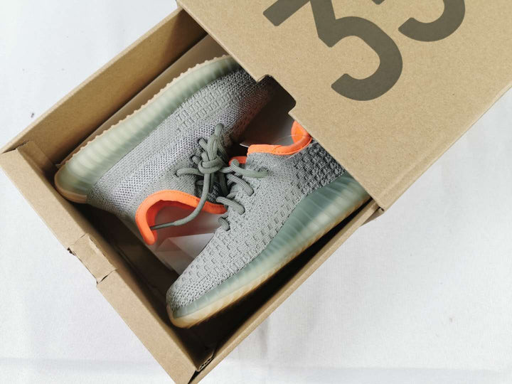 Gray and orange Yeezy 350 V2-style kids' sneakers displayed inside a cardboard shoebox.