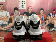 Rear view of white and black Nike-branded sneakers with gold-tone heel Swooshes and visible outsole cushioning.