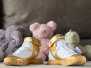 Front view of the paired high-top shoes with gold ankle straps, white uppers, and gold-toned toe areas.