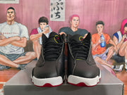 Front view of a pair of black high-top basketball sneakers with black laces, textured uppers, white toe sections, and red outsole accents.