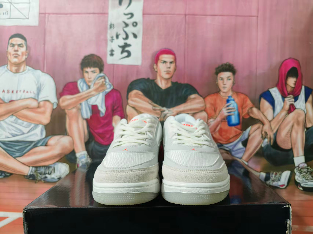 Front view of a pair of white Jordan sneakers with orange-red details, displayed on a black box.