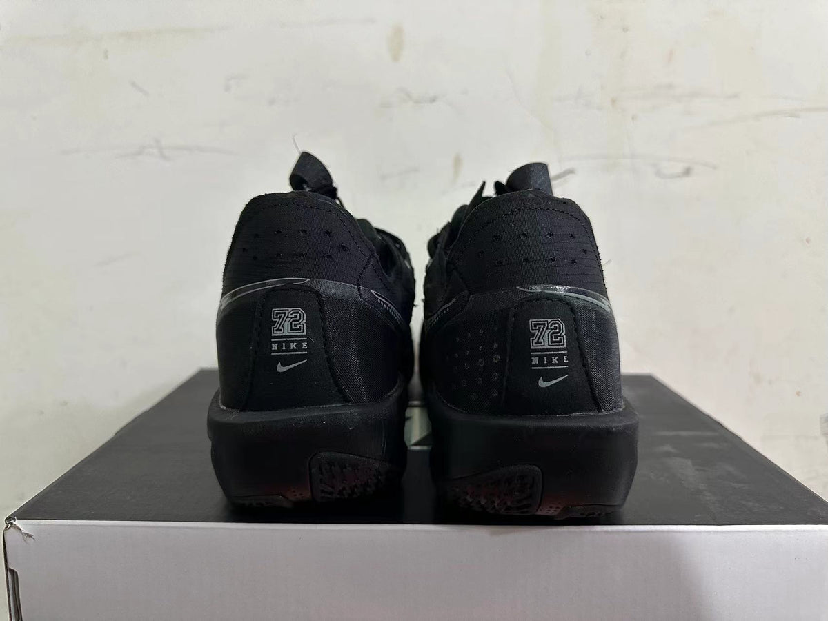 Rear view of all-black Nike sneakers showing heel branding and black midsoles