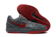 Two dark gray and red sneakers shown from the side with one outsole facing upward, revealing patterned traction.