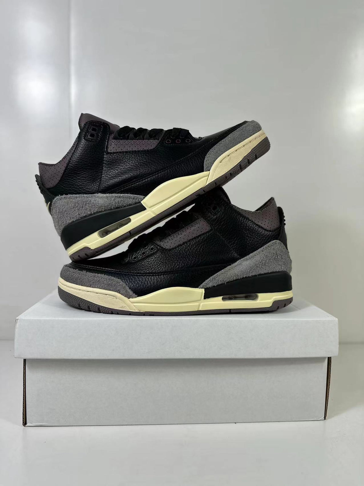 Pair of black and dark gray Air Jordan 3 sneakers with muted cream midsoles displayed on a box.