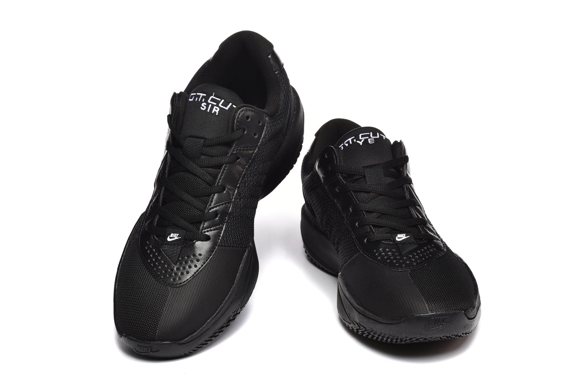 Pair of black Nike-marked low-top sneakers shown from the front, with lace-up fastening and perforated forefoot overlays.