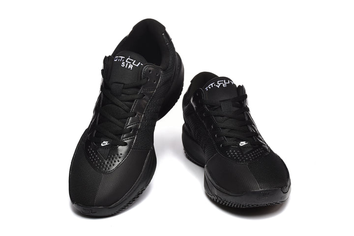 Pair of black Nike-marked low-top sneakers shown from the front, with lace-up fastening and perforated forefoot overlays.
