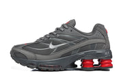Side view of a gray Nike Shox Ride 2 sneaker with mesh panels, silver-tone Swoosh, and red heel cushioning columns.