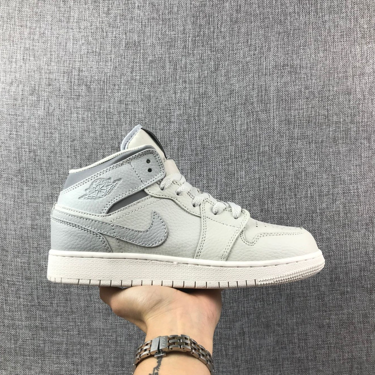 Side profile of a light bone and grey high-top Jordan sneaker with a padded collar and side Swoosh.