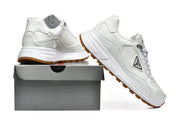 White Prada sneakers displayed beside a box, showing the side panels and gum-colored outsoles.