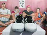 Front view of white and black GiGi basketball sneakers with gold tongue details, displayed on a white box.