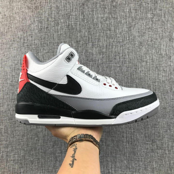 Side profile of a white, grey, black, and red Jordan Air Jordan 3 sneaker held against a grey fabric background.