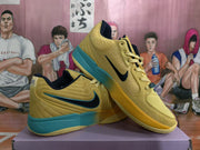 Pair of yellow basketball sneakers with blue-green midsoles and black Swooshes displayed on a box.