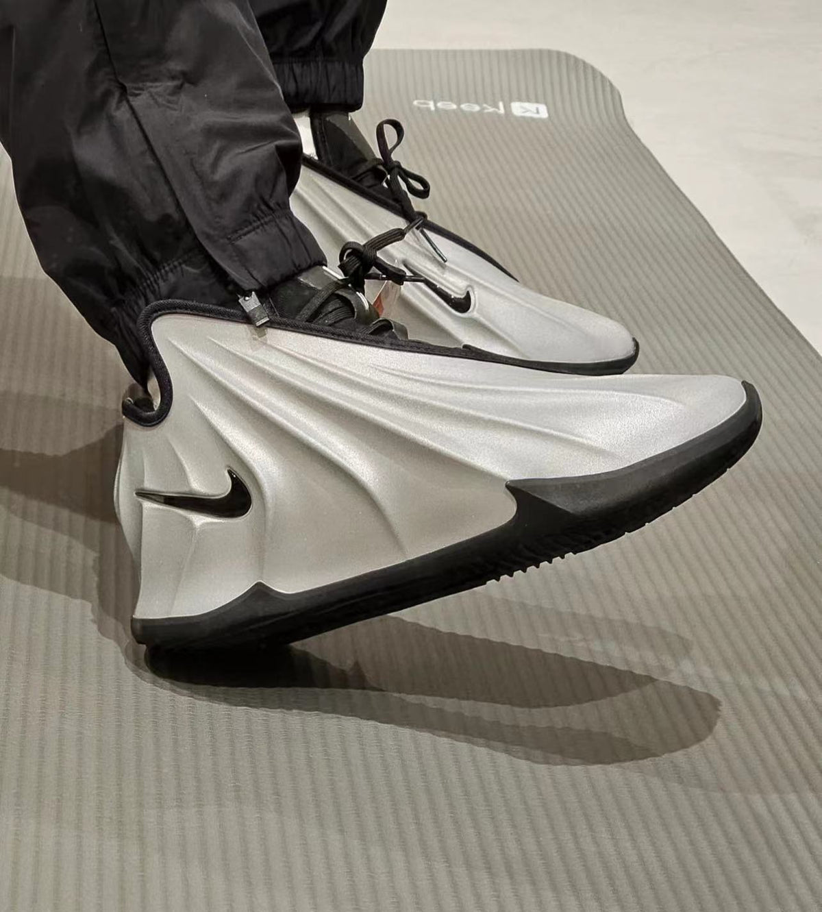 Pair of gray Nike sneakers with black Swoosh logos, black laces, and black rubber outsoles photographed on a gray surface