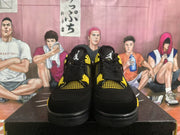 Front view of black high-top sneakers with yellow mesh panels, lace wings, and tongue logos.