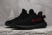 Pair of black low-top sneakers shown from the front three-quarter view with black laces and red side lettering.