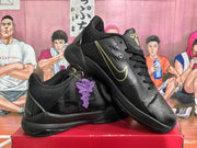 Angled view of black basketball sneakers with gold side branding, gold tongue emblems, and purple hanging accessories.
