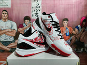 Pair of white basketball sneakers shown from an angled side and top view, highlighting the red patterned panels, black laces, and black heel details.
