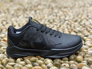 Close side profile of a black sneaker showing the perforated toe, tonal side panels, laces and black midsole.