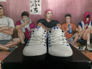 Front view of the white and blue Nike sneakers showing the lace-up design, blue tongue details, and black outsoles.
