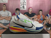 Side view of a white and gray Nike GT sneaker with a black swoosh, blue outsole edge, and yellow, orange and pink midsole accents.