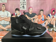 Side view of a black Nike LeBron high-top basketball sneaker with layered straps and a translucent outsole, displayed on a shoe box.