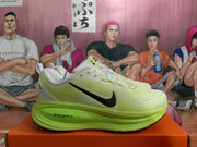 Side profile of a green Nike sneaker showing the black Swoosh, light upper, and visible ZoomX sole marking.