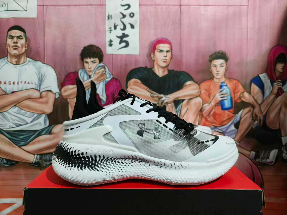 Side view of white and black Under Armour basketball sneakers on a box, showing the mesh upper, black laces, Under Armour logo, and dotted midsole.