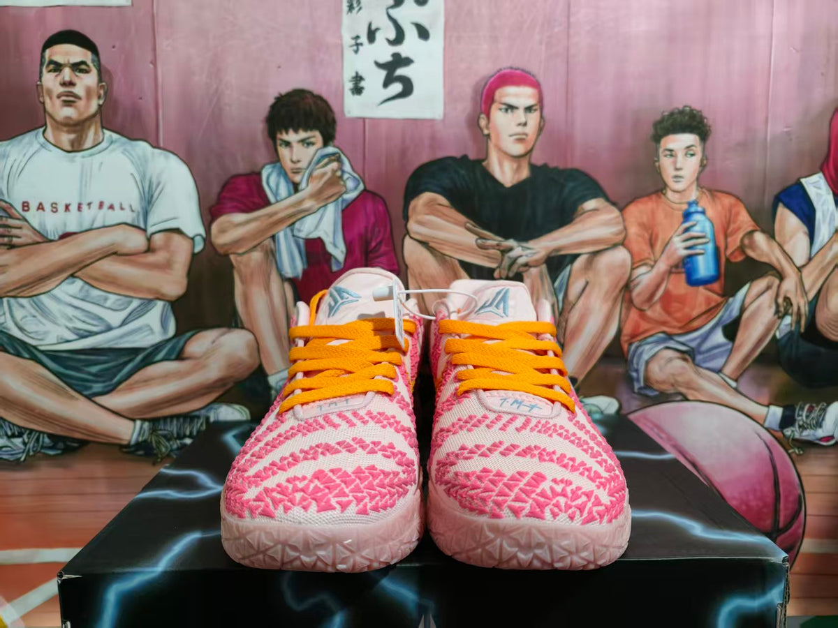 Front view of pink and pale Nike basketball-style sneakers with bright orange laces and textured pink detailing.