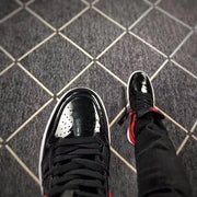 Close-up view of the glossy black perforated toe box, black laces and white midsole.