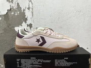 Side profile of a cream and pale pink Converse trainer-style sneaker with plum star-and-chevron emblem and gum outsole