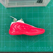 Side view of the red sneaker placed on a green cutting mat; no usable shoe size chart is visible.