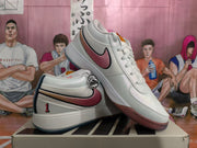Pair of white low-top sneakers displayed at an angle, showing pink Swooshes and blue accents.