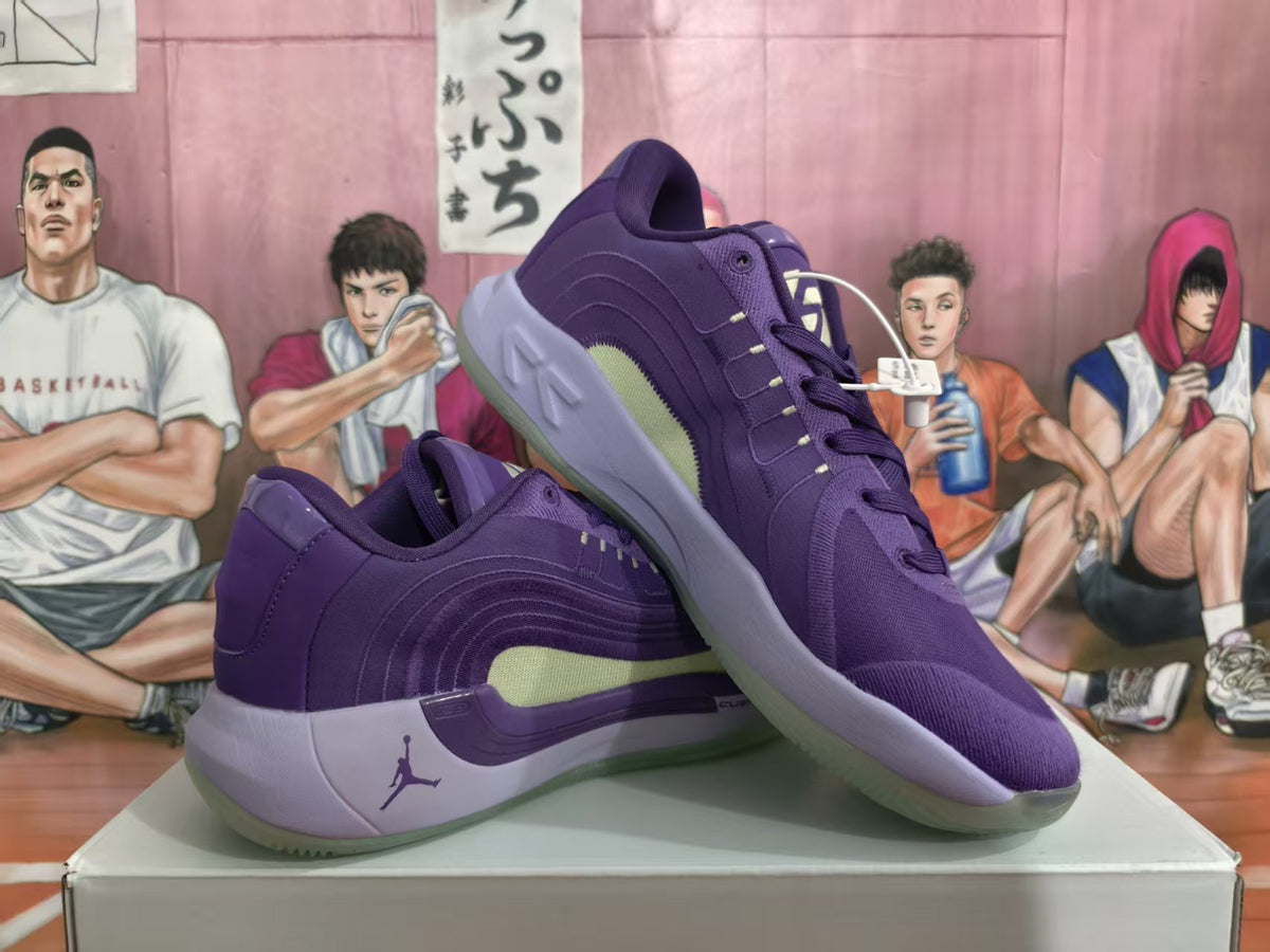 Pair of purple Jordan basketball sneakers shown from a three-quarter side angle, with green side panels and translucent outsoles.
