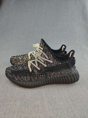 Side view of black 350 V2-style sneakers showing the textured upper, contrasting laces, ribbed outsole, and rear pull tabs.