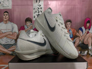 Pair of grey Nike basketball shoes shown from the side, with black Swooshes and sculpted soles.
