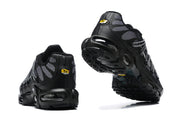 Rear and outsole views of black and grey Nike Air Max Plus sneakers with Tn heel badges.