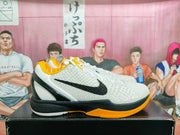 Side view of a white textured basketball sneaker with black branding, gold outsole accents, and a black heel.