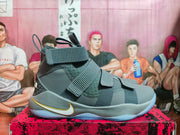 Side view of a grey Nike basketball shoe with adjustable straps and white-and-gold Swoosh.