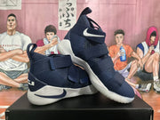 Angled view of two navy blue Nike basketball sneakers showing the side Swooshes, layered straps, high-top collars, and light-colored soles.