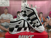 Angled view of white, black, and grey Nike Air More Uptempo sneakers showing the side lettering and chunky sole.