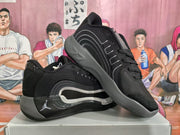 Angled view of a pair of black and gray Jordan basketball sneakers showing the lace-up construction, padded collars, and gray midsoles.