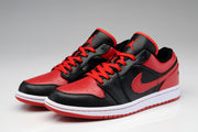 Front three-quarter view of the black and red low-top sneakers with red laces and tongue branding.