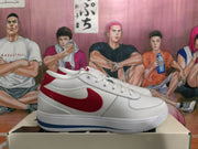 Side view of a white sneaker with a red Nike Swoosh, red heel detail, and blue outsole accent.