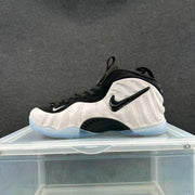 Single white and black Foamposite-style sneaker shown from the lateral side, with black swoosh and light-blue translucent outsole.