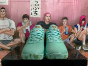 Front view of mint green basketball sneakers with brown-gold tongue accents on a black box.