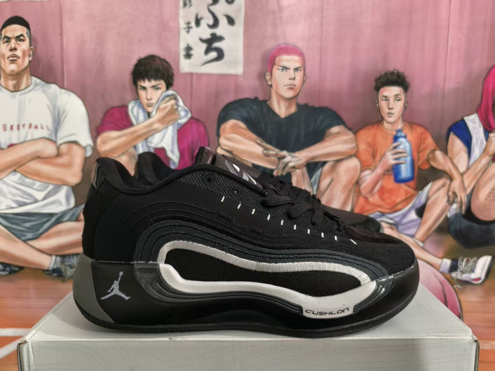 Side view of a black and gray Jordan basketball sneaker on a box, showing layered side panels, light trim, and visible Jumpman branding.