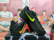Three-quarter view of black Nike basketball sneakers showing neon green and orange swoosh accents, textured uppers, and black outsoles.