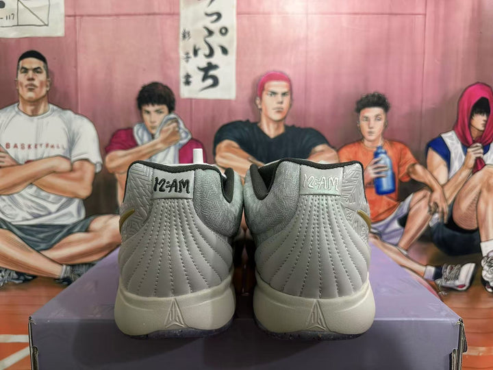 Rear view of light gray-white Nike basketball shoes with “12AM” heel tabs and dark speckled outsoles.