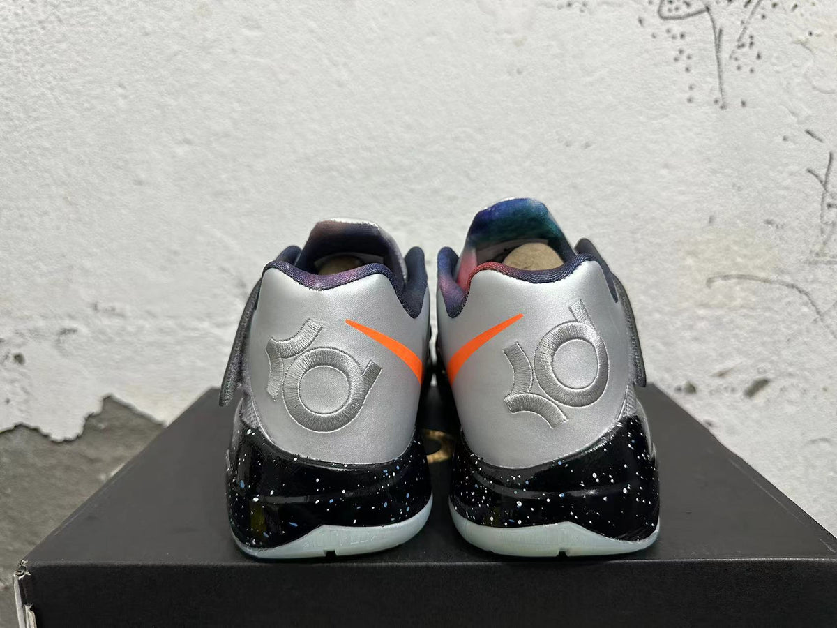 Rear view of silver Nike KD basketball shoes with orange accents and a black speckled midsole.
