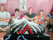 Side view of a white basketball shoe with black geometric patterning, red accents, and a black outsole.